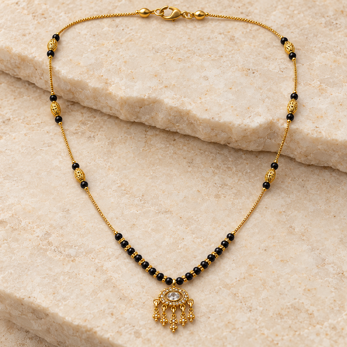 A gold and black beaded necklace with a dangling ornate gold pendant, displayed on a light beige stone surface.