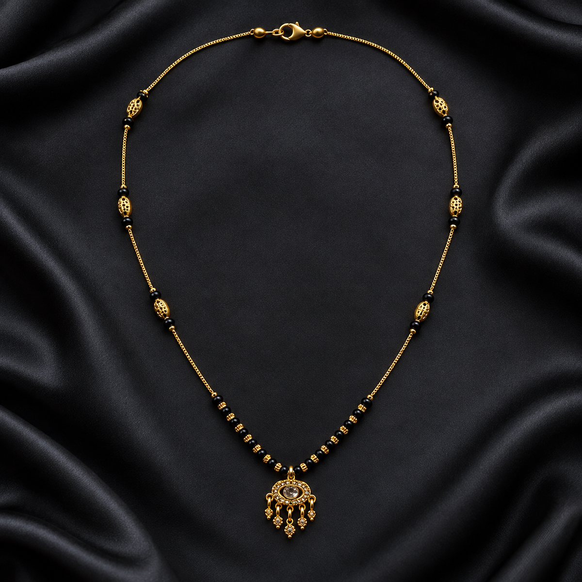 A gold-toned beaded necklace with a detailed pendant, displayed on a draped black satin fabric background.