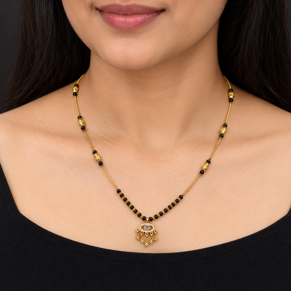 A close-up of a woman wearing a gold and black beaded necklace with a decorative gold pendant featuring a white and black eye motif, set against a dark background.