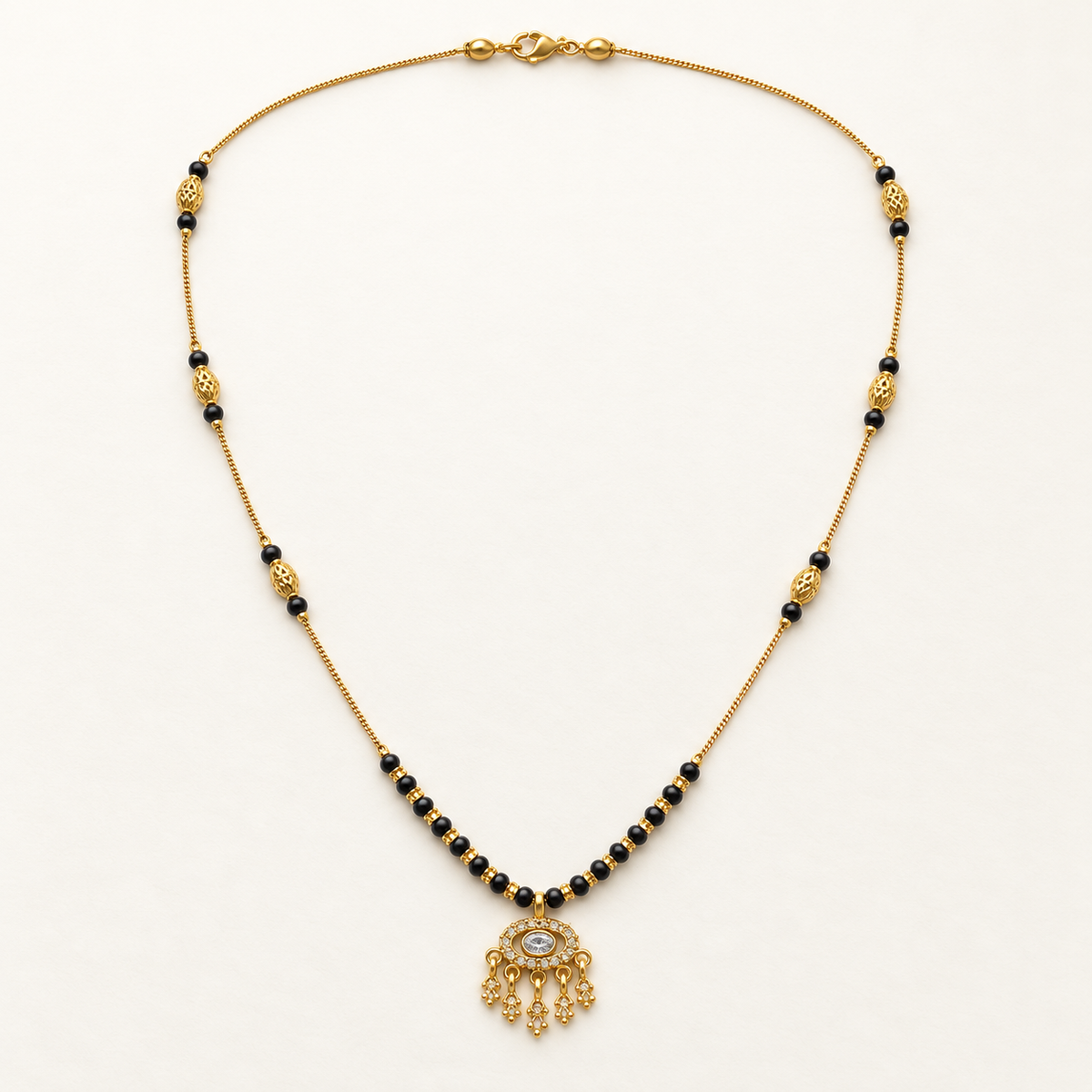 A gold chain necklace with small black beads, decorative gold spacer beads, and a dangling ornate gold pendant featuring a central clear stone, displayed on a clean white background.