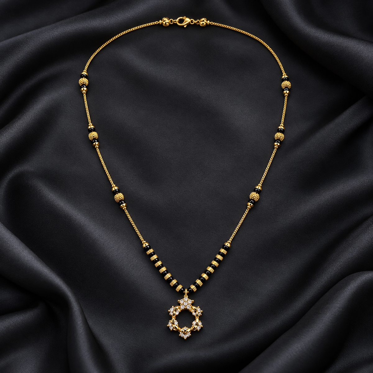 A gold-toned beaded necklace with a circular pendant set with clear stones, displayed on draped black satin fabric.
