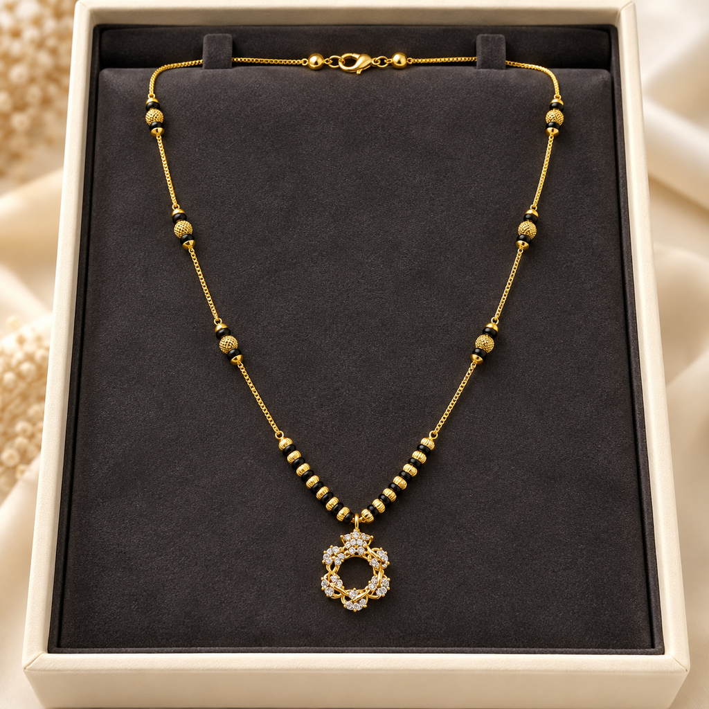 A gold-toned beaded necklace with a circular pendant set with clear stones, displayed on a black velvet jewelry box insert inside a cream-colored box.