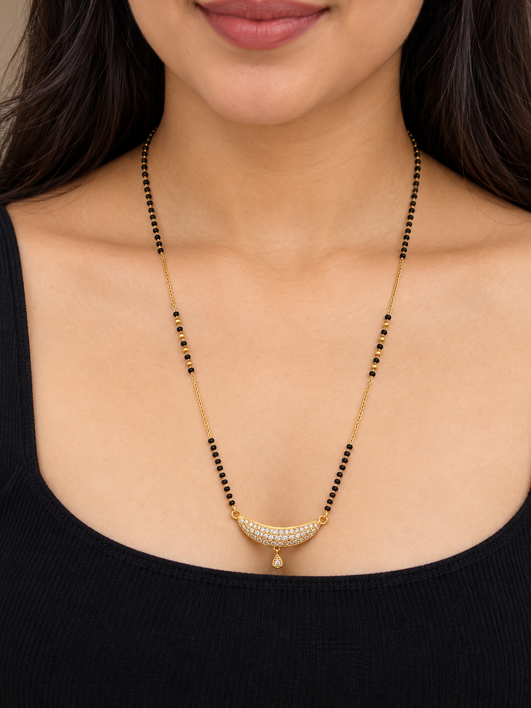 A close-up of a woman wearing a gold and black beaded necklace with a crescent-shaped pavé pendant.