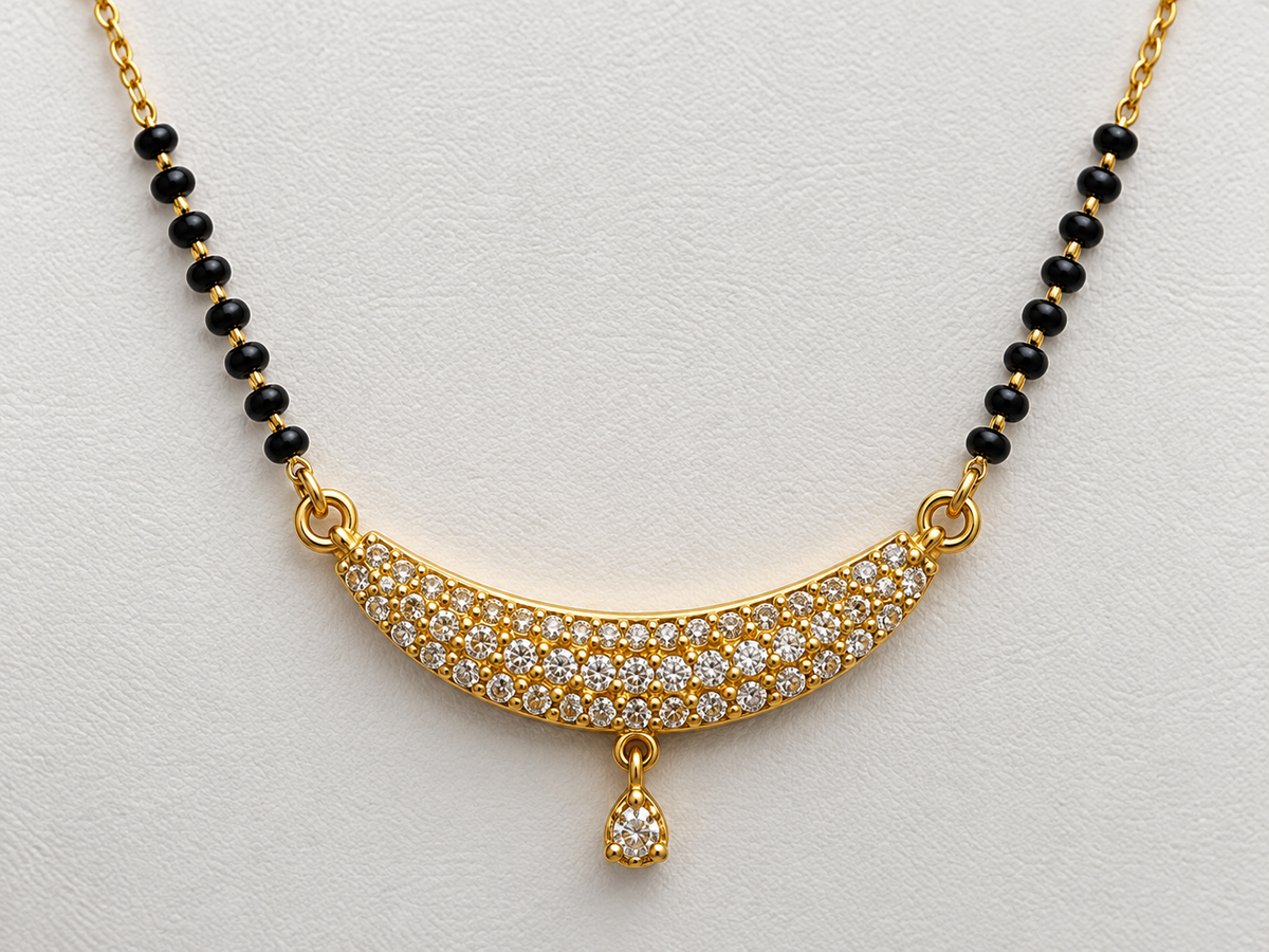 Gold necklace with a curved pavé pendant set with clear stones, flanked by black bead sections on a white textured background.