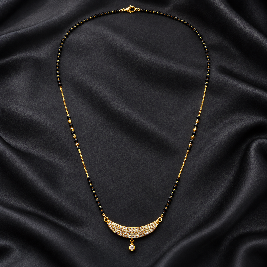 A gold-tone necklace with a crescent-shaped pavé pendant and a teardrop drop, laid out on a draped black satin fabric background.
