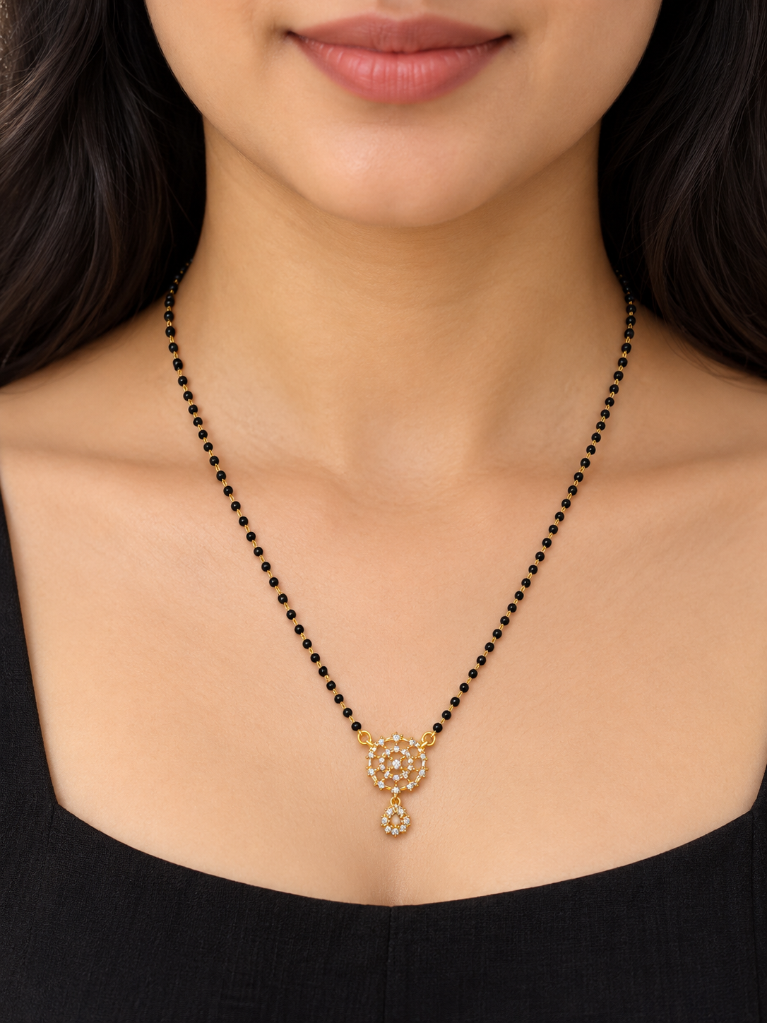 A close-up of a woman wearing a black beaded necklace with a gold-toned pendant adorned with small clear stones.