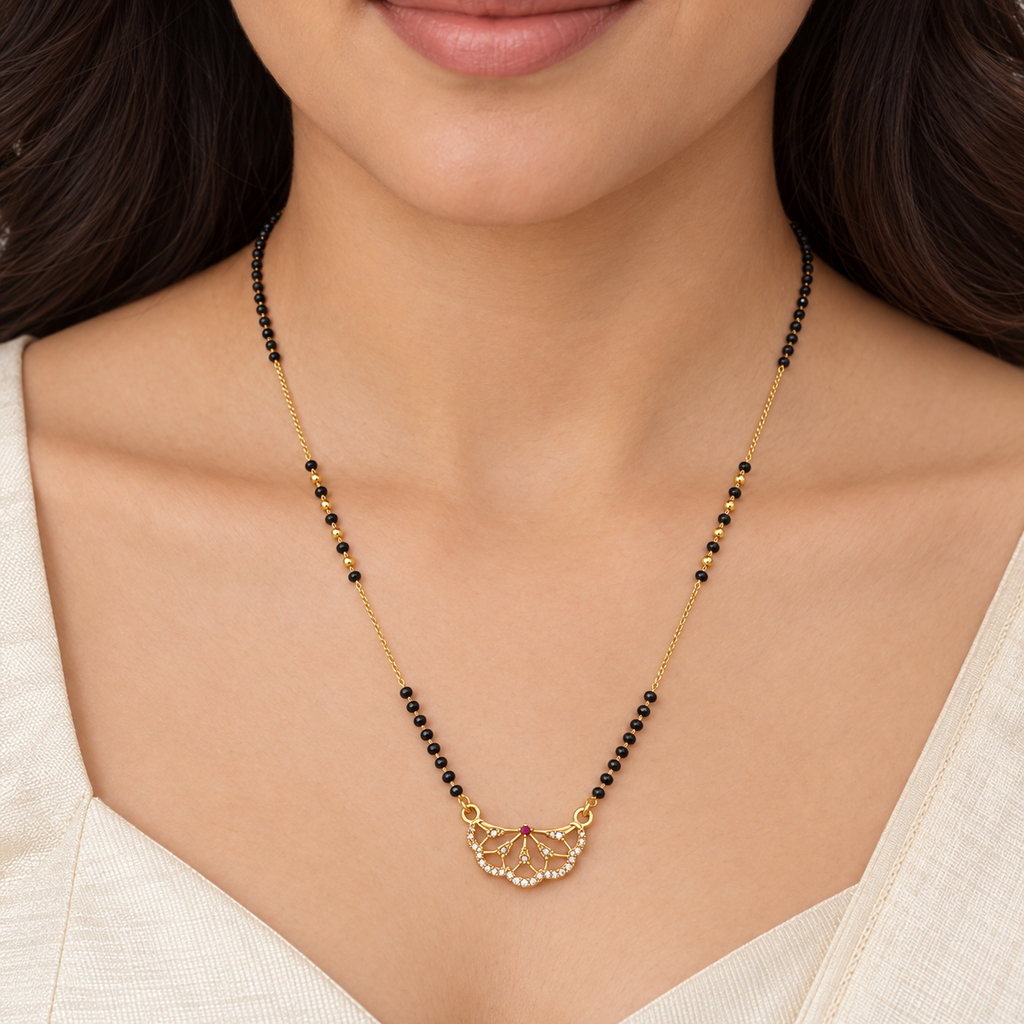 A close-up of a woman wearing a delicate gold necklace with small black beads and a gold pendant, paired with a light beige top.