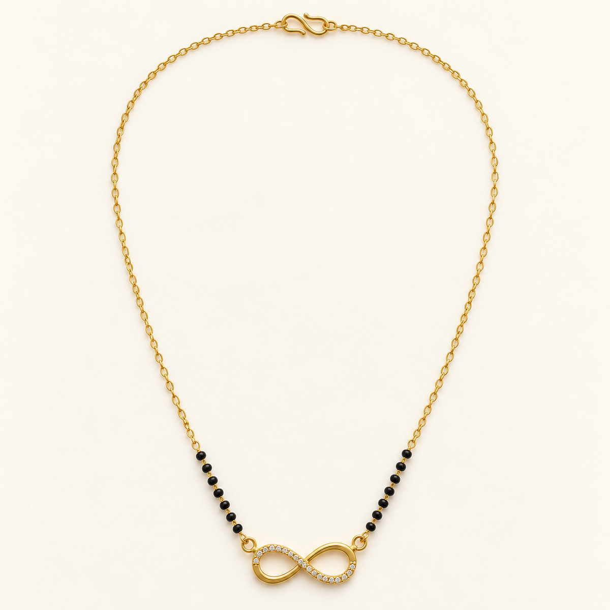 A gold chain necklace featuring a central infinity symbol paved with small clear stones, flanked by strands of small black beads, on a light cream background.