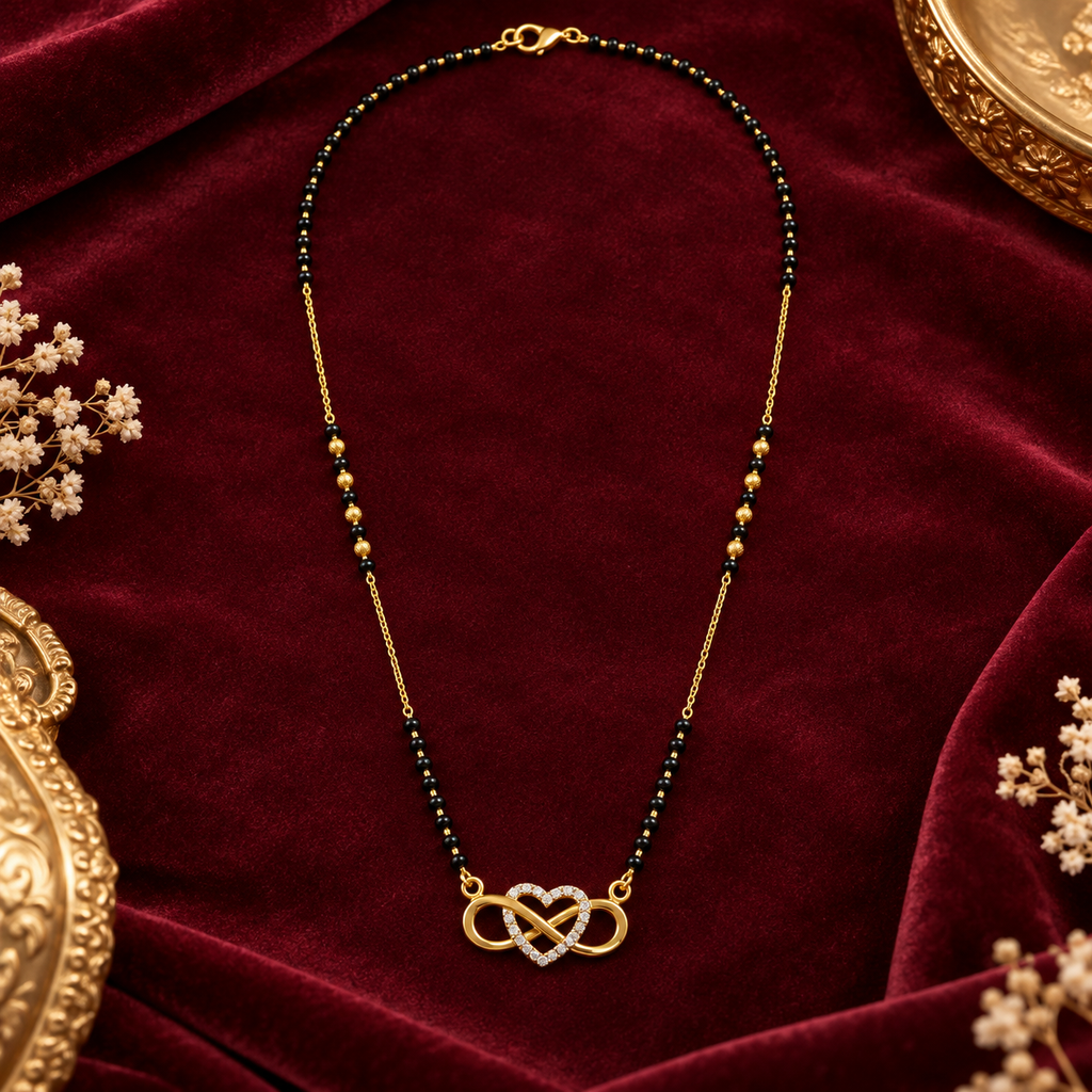 A gold chain necklace with a heart-shaped infinity symbol set with small clear stones, accented by dark green and gold beads, displayed on a deep red velvet background with decorative gold frames and dried flowers.