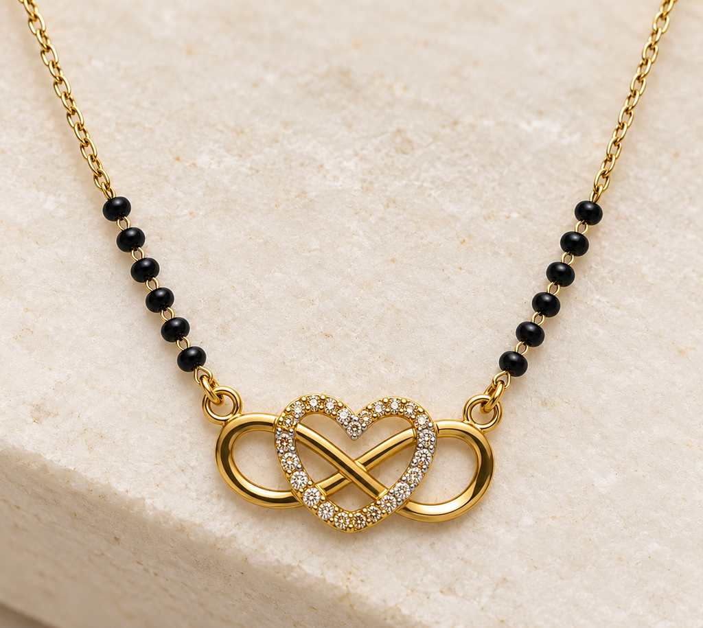 Gold chain necklace with a heart-shaped infinity symbol adorned with small clear stones, connected by a gold infinity loop, and accented with black beads on the chain, displayed on a light beige stone surface.