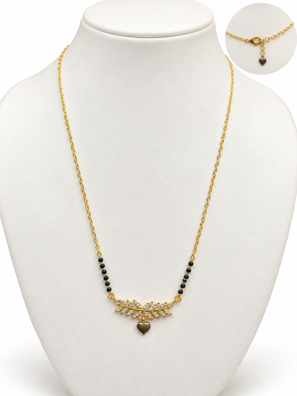 Gold chain necklace with a central gold leaf-like pendant set with small clear stones, flanked by black beads, displayed on a white mannequin bust. An inset circle in the top right shows the clasp detail.
